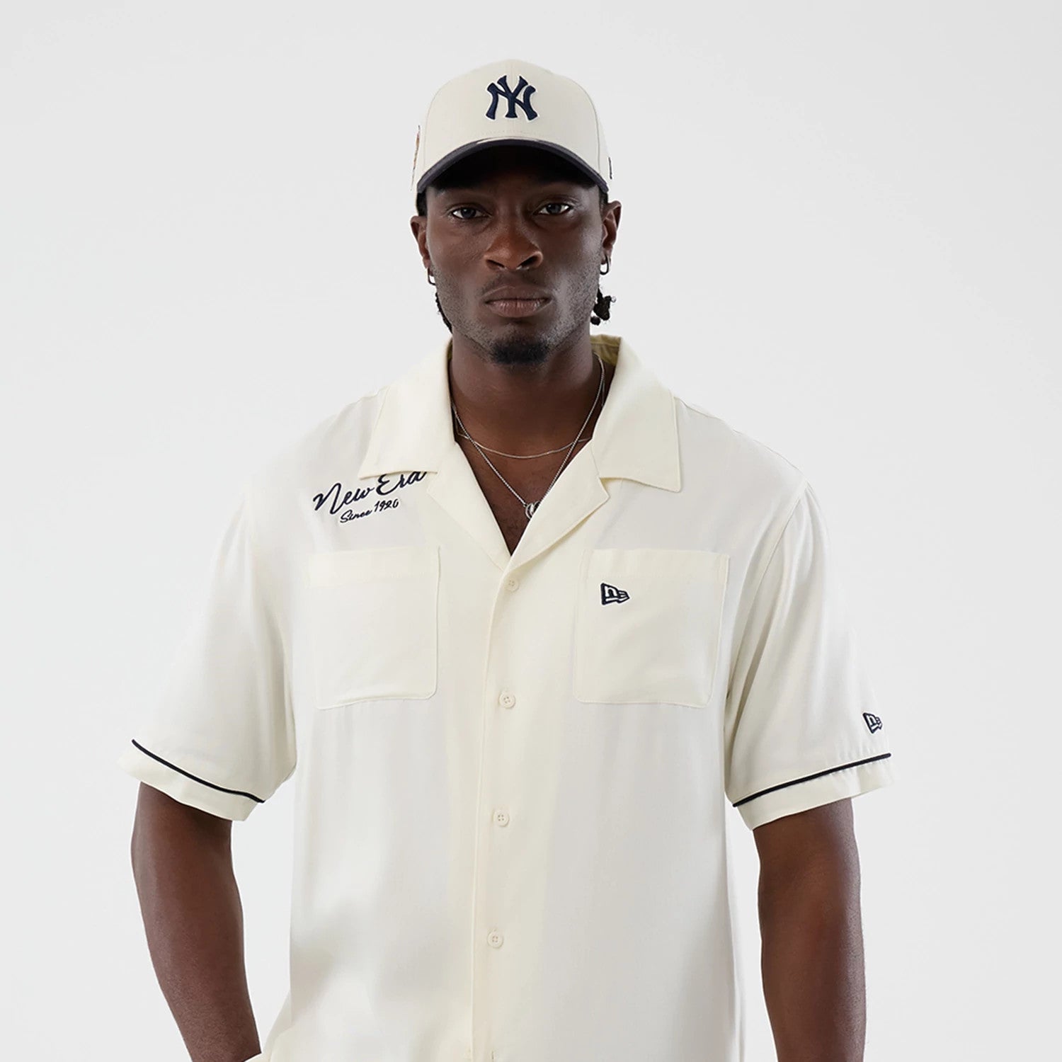 The model is wearing this New Era Graphic Revere Short Sleeve Shirt in open white. 3