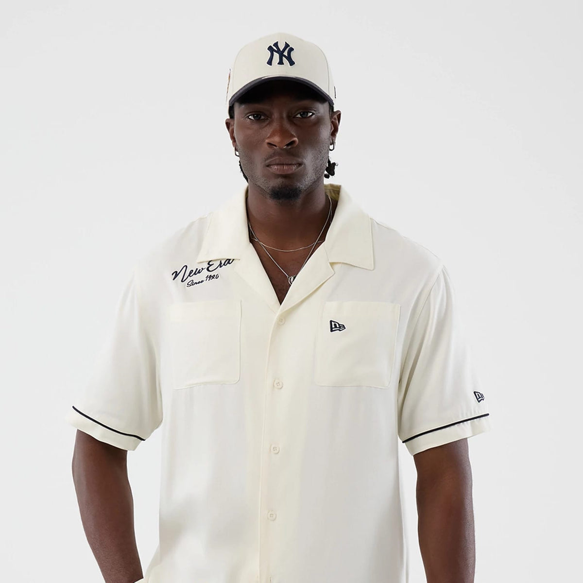 The model is wearing this New Era Graphic Revere Short Sleeve Shirt in open white. 3