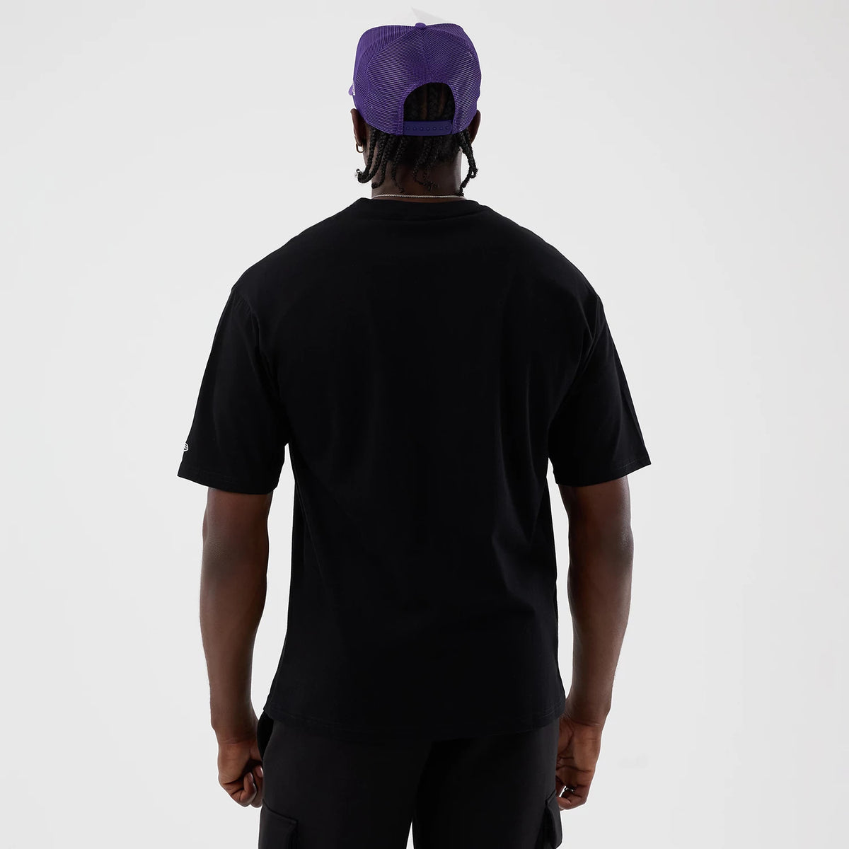 New Era LA Lakers NBA Basket Made Black Oversized T-Shirt, back view on a model wearing a purple cap, displaying a plain black rear with a small embroidered New Era logo on the lower sleeve, and relaxed fit sleeves.