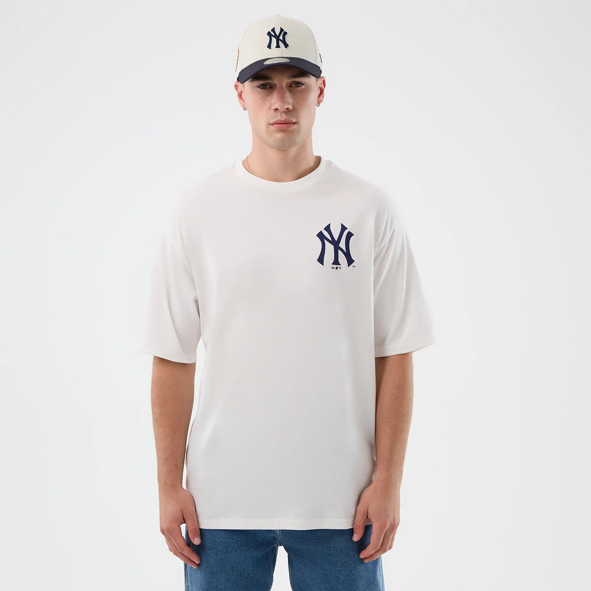 New Era New York Yankees MLB Cap Graphic White Oversized T-Shirt, front view on a model wearing a matching cap, featuring a large navy embroidered New York Yankees logo on the left chest and short sleeves with a loose fit.