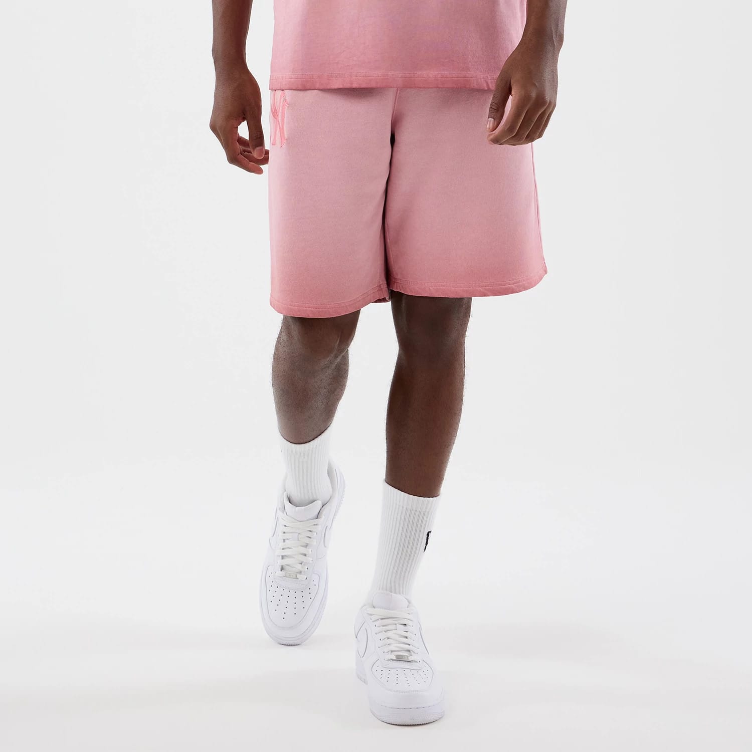 New Era New York Yankees MLB Washed Logo Pastel Pink Shorts, front view on-model showing pastel pink shorts with a gradient effect, embroidered New York Yankees logo near the waistband and drawstrings on the left side, paired with white trainers.