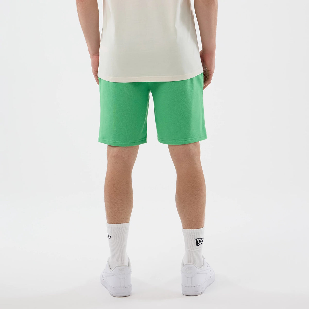 New Era LA Dodgers MLB League Essential Open Green Shorts, back view on a model styled with a white shirt and trainers, showing the green colour extending smoothly to the hem, prominently contrasting against the white New Era logo on the socks.