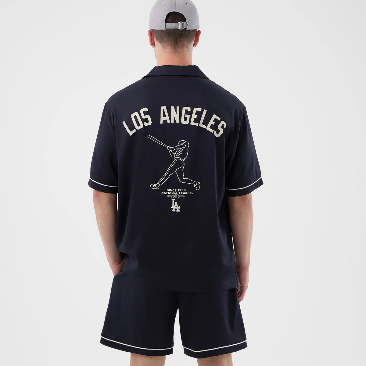 New Era LA Dodgers MLB Graphic Revere Navy Short Sleeve Shirt, back view on a model showing large LOS ANGELES lettering across the shoulders, an outline of a baseball player mid-swing below, and an LA logo with accompanying text at the lower back.