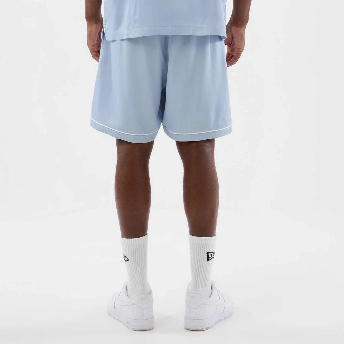New Era New York Yankees MLB Woven Pastel Blue Shorts, back view showing the light blue shorts with white piping along the hem, worn by a model styled with white sneakers and socks featuring the New Era embroidered logo above the ankle.
