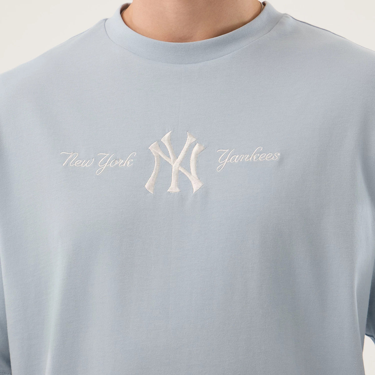 New Era New York Yankees MLB Script Pastel Blue Oversized T-Shirt, front view highlighting the light blue fabric with an embroidered white New York Yankees logo centred on the chest, flanked by elegant script New York and Yankees lettering.
