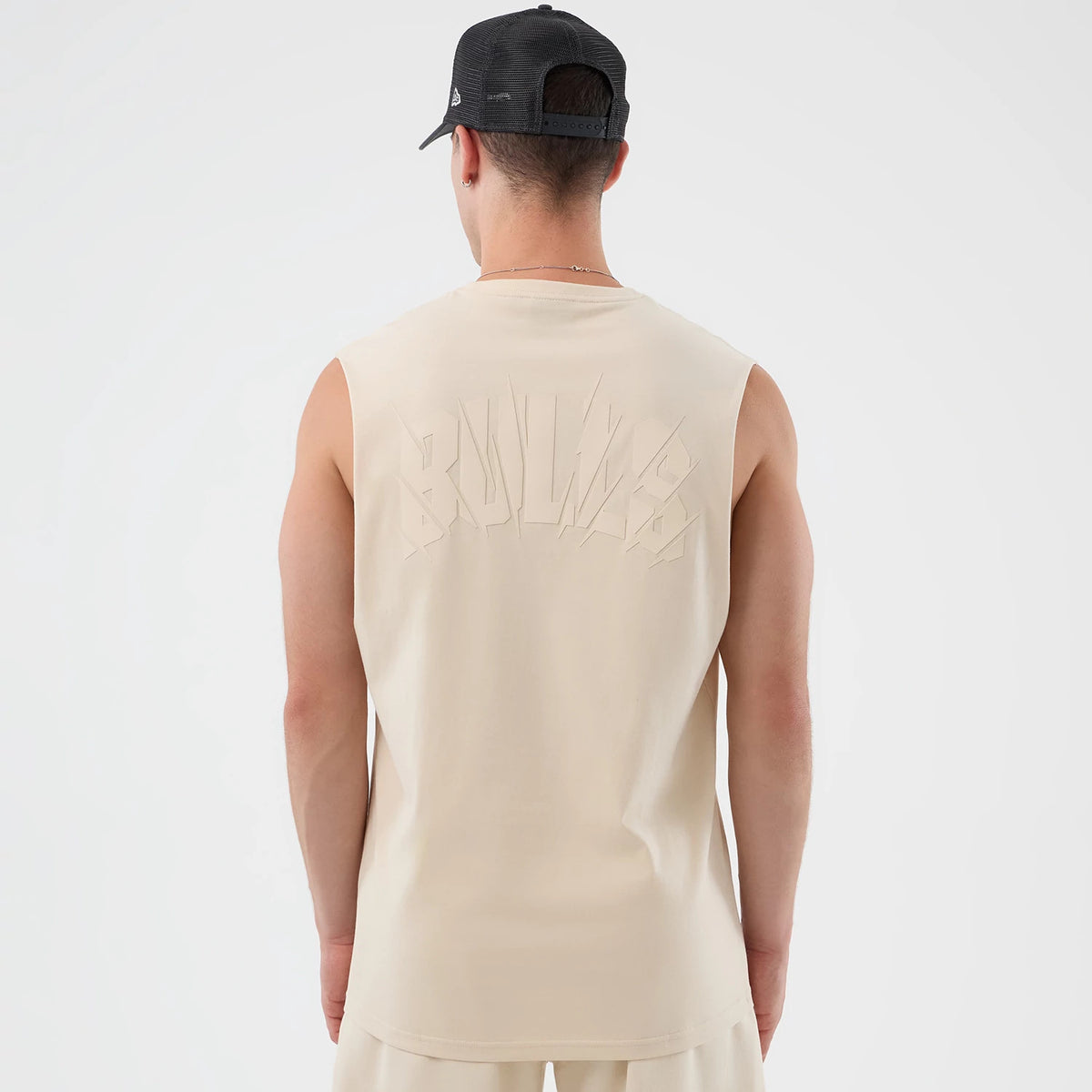 New Era Chicago Bulls NBA Core Plus Light Beige Vest, back view on a model with a black cap, featuring 'BULLS' lettering in light beige across the upper back, sleeveless design emphasising athletic arms, and a longline cut for a fit.