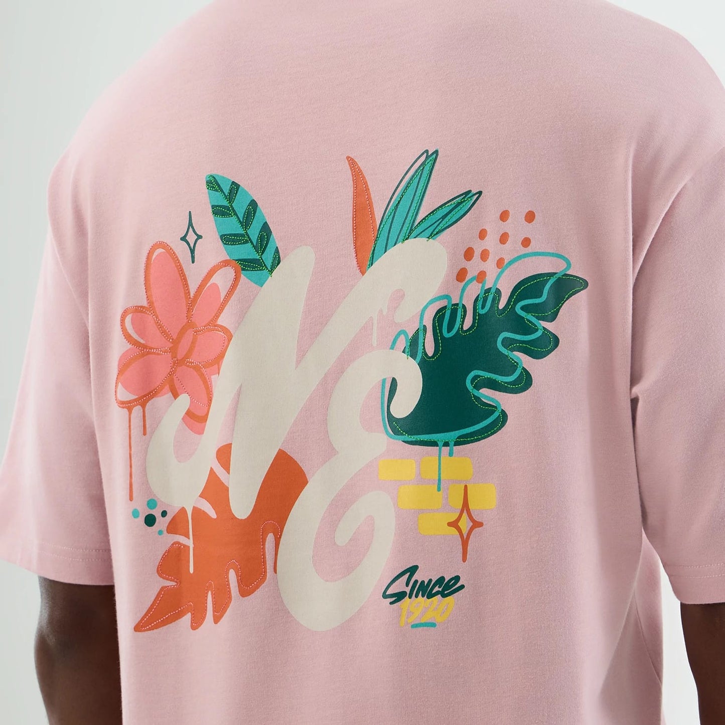 New Era Floral Graphic Pastel Pink Oversized T-Shirt, back view showing a floral graphic with stylised NE lettering, large green and orange leaves, pink and orange flower motifs, and 'Since 1920' text printed at the bottom.