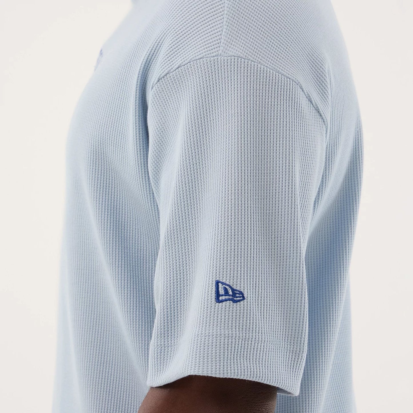 New Era LA Dodgers MLB Waffle Pastel Blue T-Shirt, side view showing the textured waffle pattern on the light blue fabric, with a navy blue embroidered New Era logo near the cuff on the short sleeve.