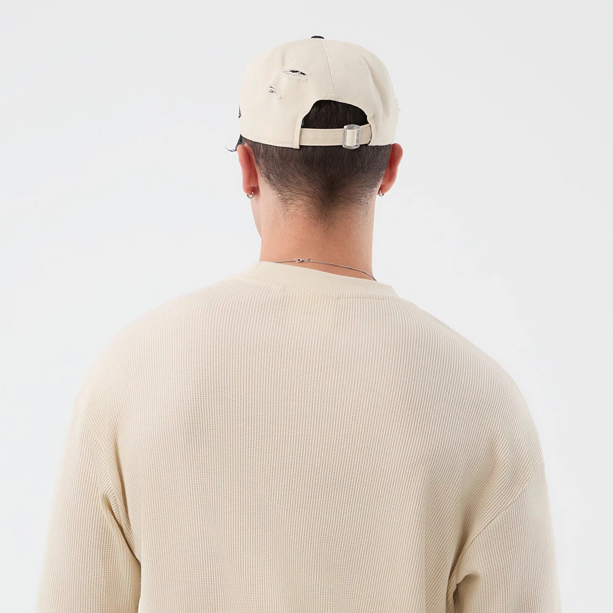 New Era Waffle Light Beige T-Shirt, back view on a model showing the textured waffle pattern of the light beige fabric, complemented by a matching cap with distressed details, and an adjustable strap at the back of the cap.