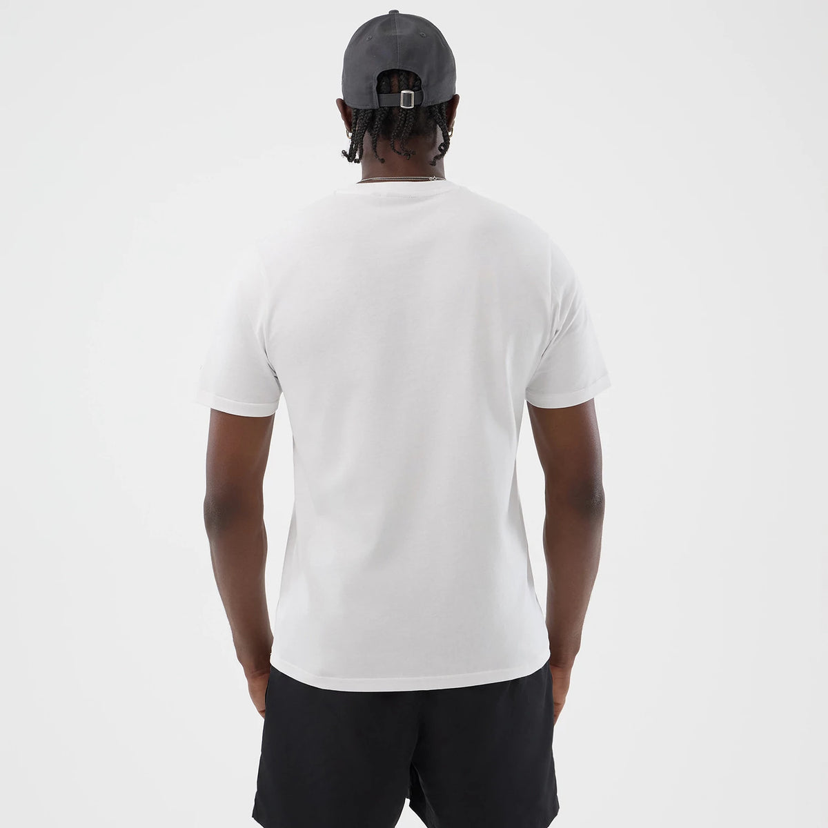 New Era Logo Graphic White T-Shirt, back view on a model, showcasing the plain white surface of the shirt, short sleeves, and a clean neckline, styled with black shorts and a grey cap from the rear angle.