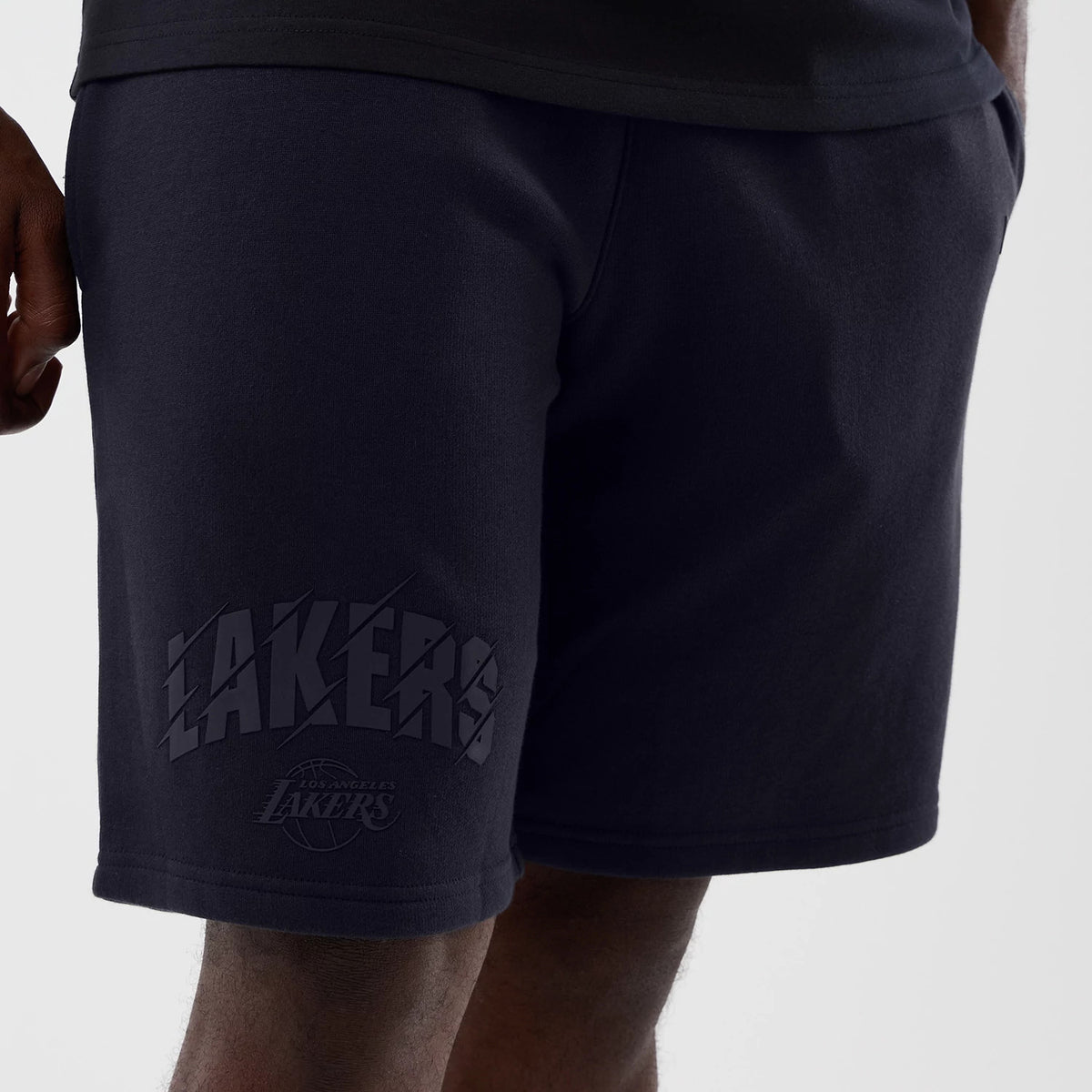 New Era LA Lakers NBA Core Plus Navy Shorts, front view on a model showcasing shadowed LAKERS lettering embossed on the left leg above the knee, combined with a Los Angeles Lakers logo beneath for added team spirit.
