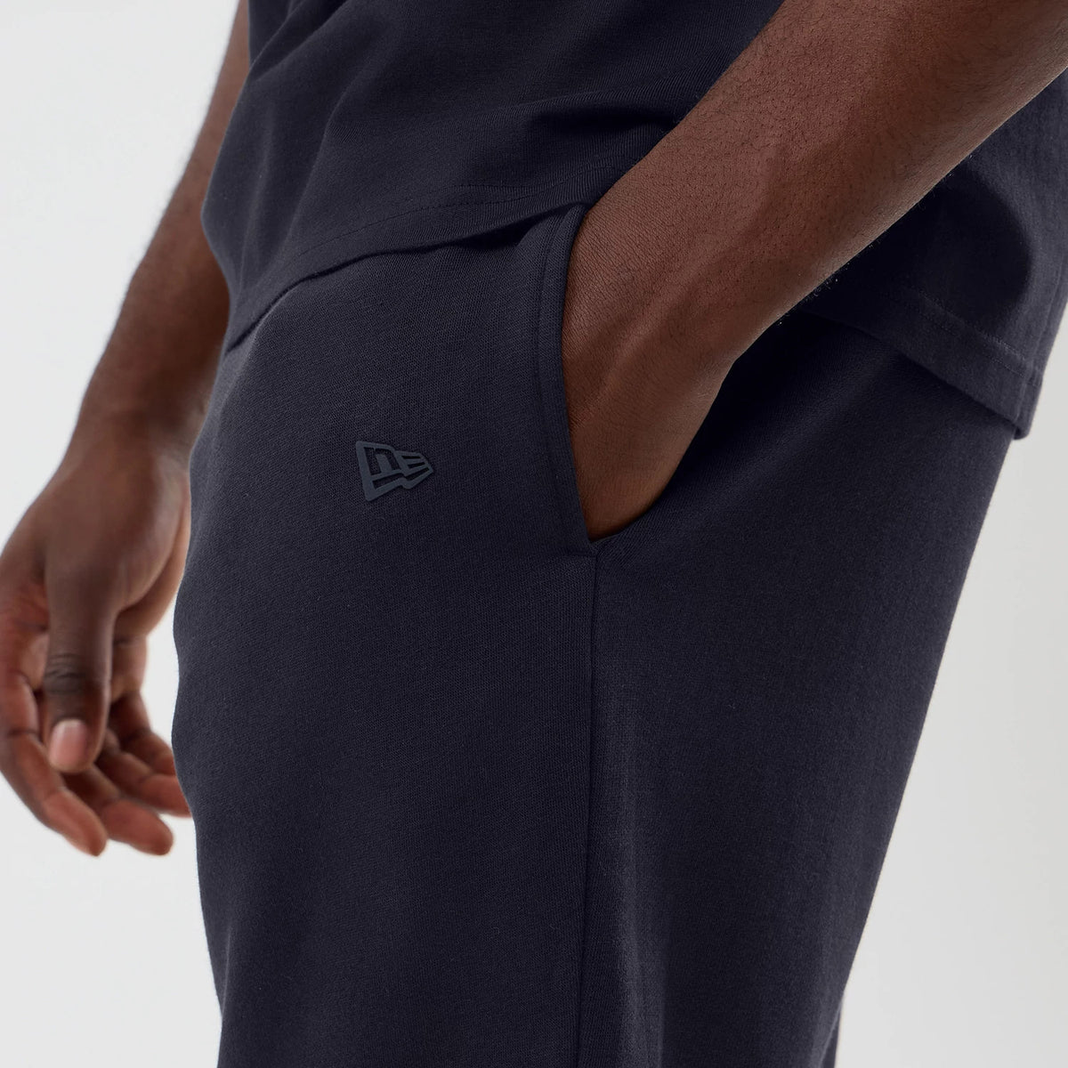 New Era LA Lakers NBA Core Plus Navy Shorts, side view showing a raised New Era logo near the left pocket, the deep navy colour, and tapered leg, styled on a model with hands casually positioned.