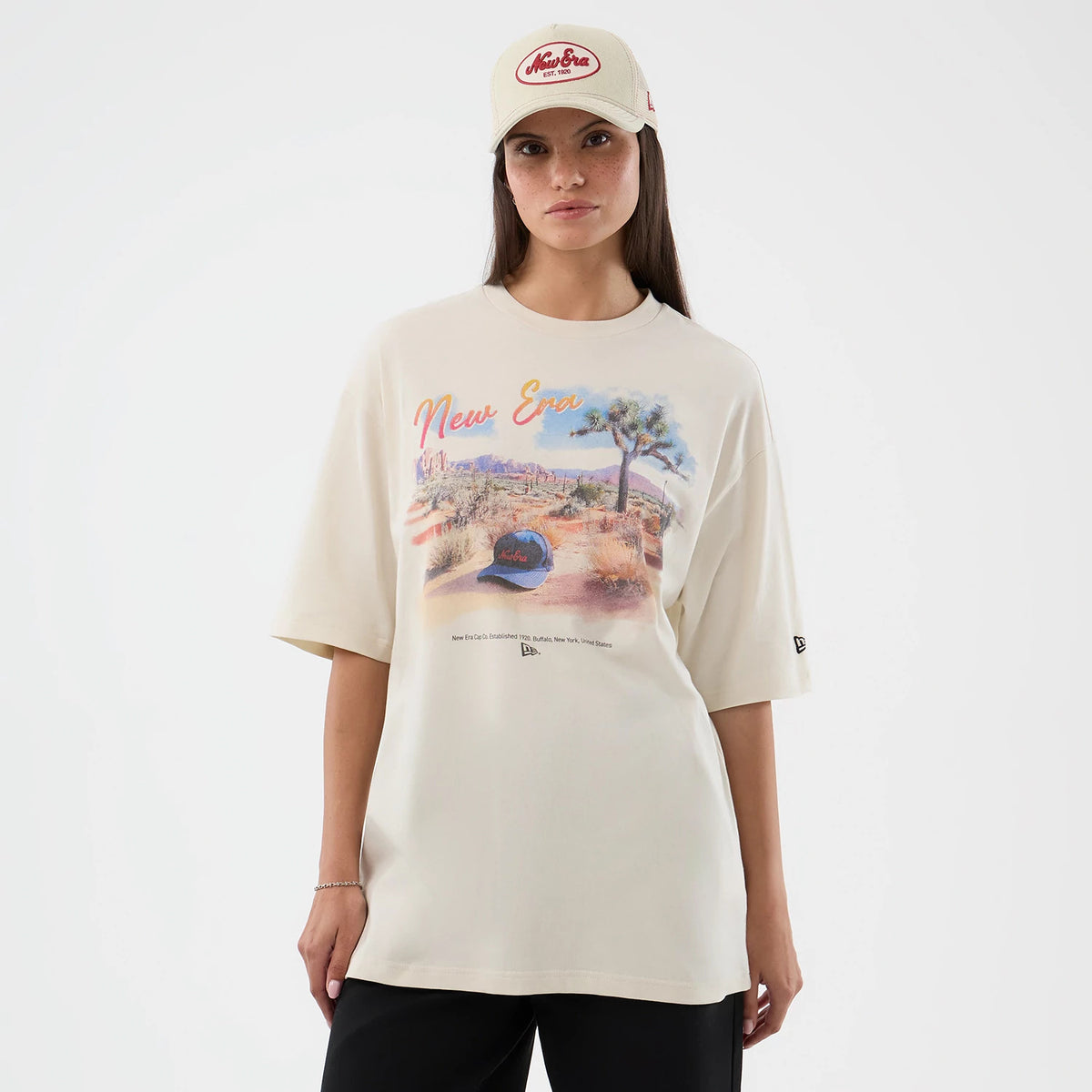 New Era Dessert Graphic Light Beige Oversized T-Shirt, front view on-model showing a colourful desert landscape graphic with a New Era cap image centred on the chest, embroidered New Era logo on the left sleeve.