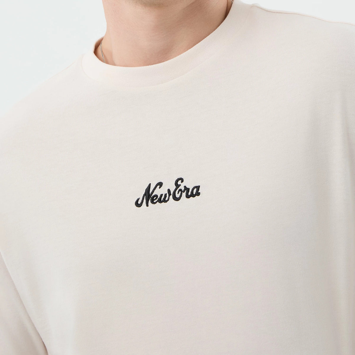 New Era Floral Graphic Open White Oversized T-Shirt, front view showing a black embroidered New Era logo centred on the chest, with a close-up of the round neckline and the white fabric backdrop, worn on a upper torso.