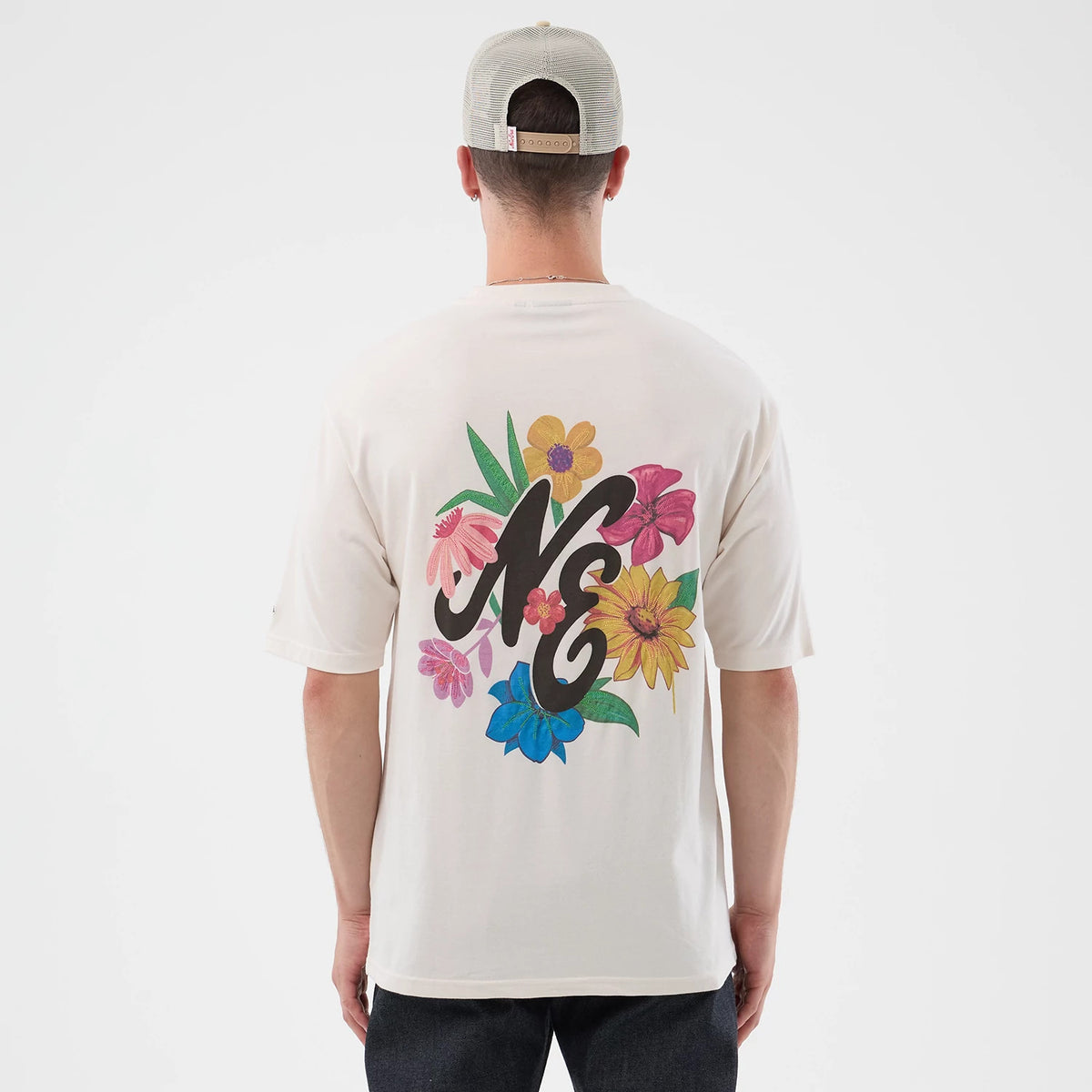 New Era Floral Graphic Open White Oversized T-Shirt, back view on a model showing a black NE logo surrounded by multicoloured flowers including pink, yellow, and blue petals, set against a plain white backdrop.