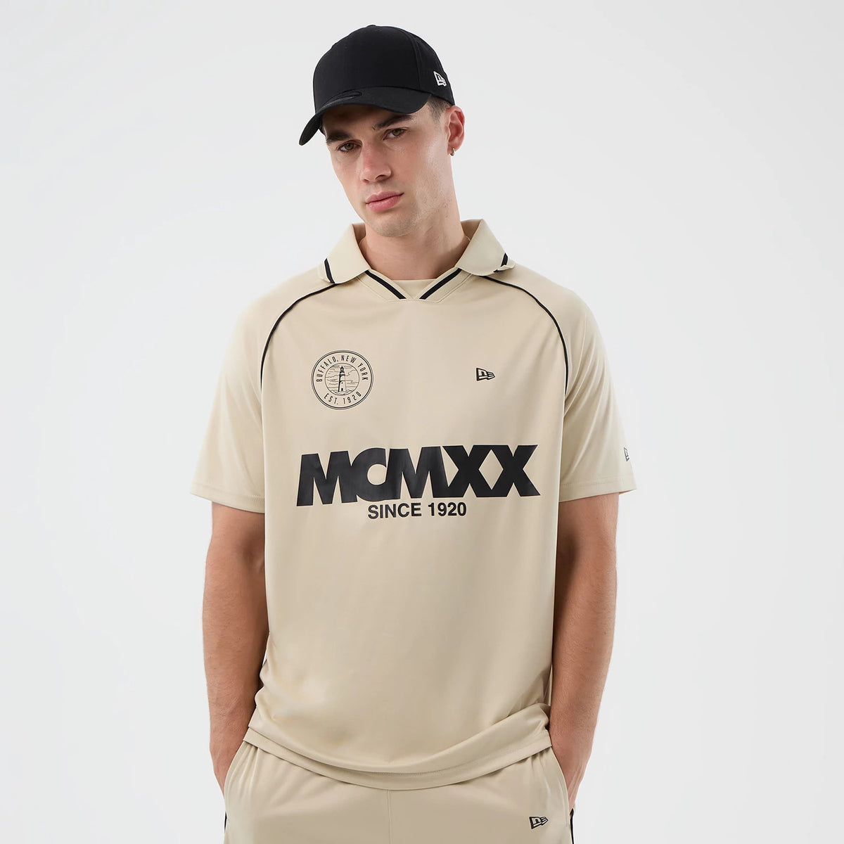 New Era Football Light Beige T-Shirt, front view on-model displaying a circular black printed logo near the left shoulder and MCMLXX lettering with Since 1920 below it on the chest, and a small embroidered New Era logo on the right.