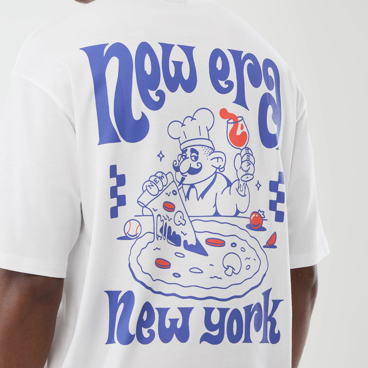 New Era Fun Pizza Graphic White Oversized T-Shirt, back view on a model showing a blue and red graphic featuring a cartoon chef holding a pizza and a glass of wine, with large curved New Era lettering above and New York below.