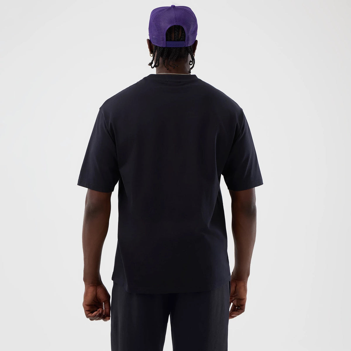 New Era LA Lakers NBA Core Plus Navy Oversized T-Shirt, back view on a model, plain navy back with a straight hem finishing around hip level, styled with a purple cap and matching navy shorts.
