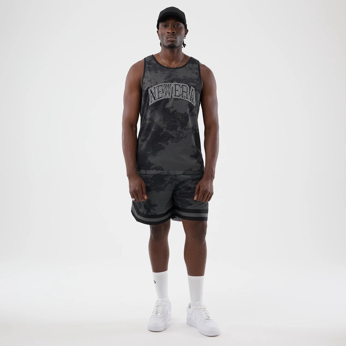 New Era All Over Print Black Camo Mesh Tank Top, front view on a model featuring a NEW ERA lettering across the chest in white, a black camo pattern throughout the mesh fabric, and sleeveless design offering a relaxed fit.