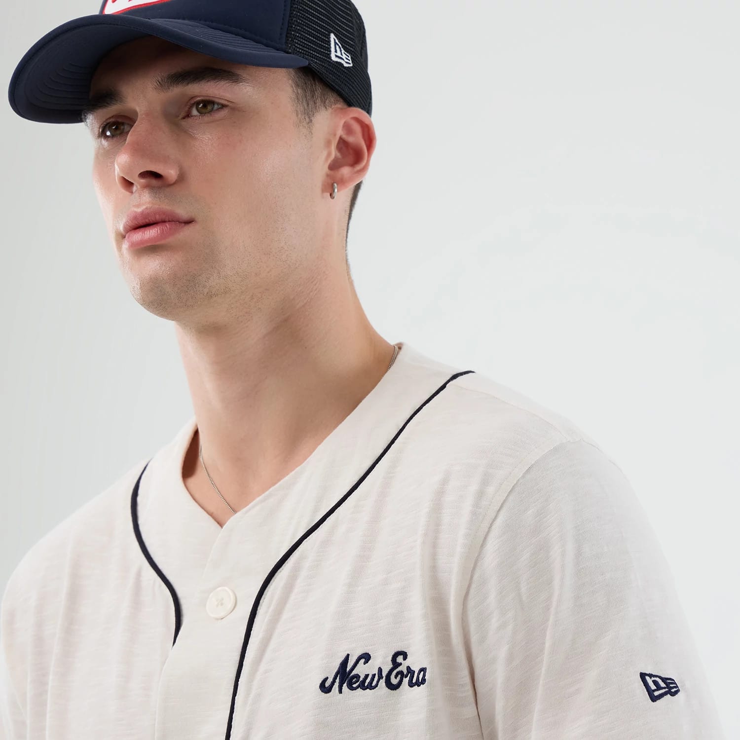 New Era Slub Open White Baseball Jersey, on-model view showing the embroidered New Era script on the left chest, button closure, and contrasting navy piping along the placket and neckline with an additional New Era flag logo on the left sleeve.