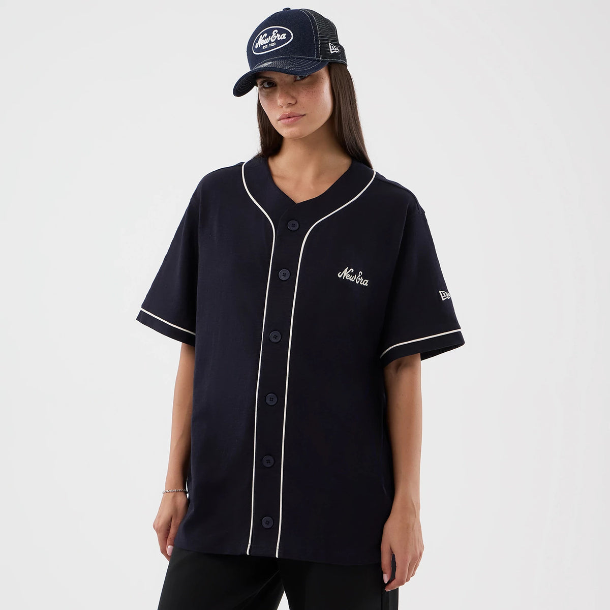 New Era Slub Navy Baseball Jersey, front view on a model showing white piping along the placket and collar, the embroidered New Era script logo on the left chest, and a white New Era flag logo on the left sleeve.