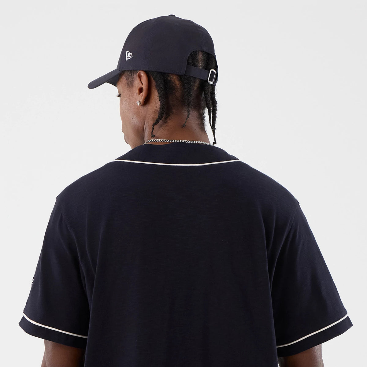 New Era Slub Navy Baseball Jersey, rear view on a model with a navy cap featuring the New Era flag logo on the left side, showing white piping along the neckline and sleeve ends, highlighting the elegant slub texture.