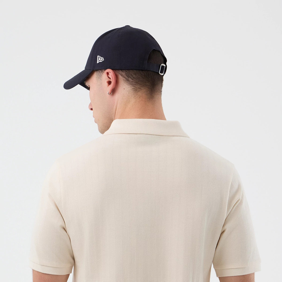 New Era LA Dodgers MLB Rib Open White Polo T-Shirt, back view on a model paired with a dark cap featuring an embroidered New Era logo on the side, showcasing the polo's raised rib texture and finished collar with short sleeves.