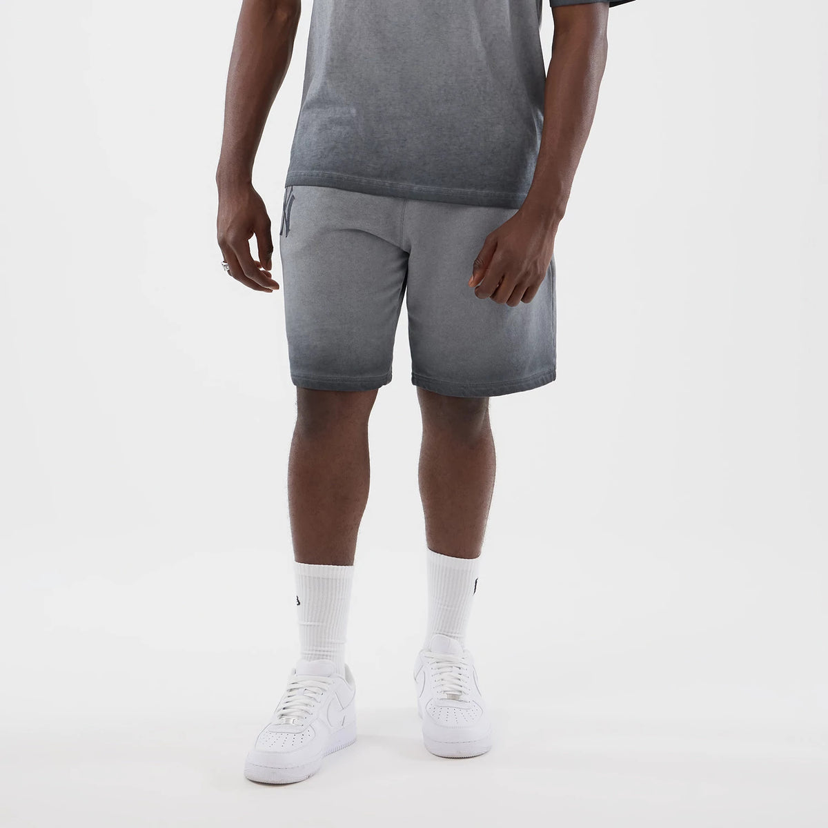New Era New York Yankees MLB Washed Logo Black Shorts, front view on a model wearing white trainers and socks, showing a gradient effect from grey to black with an embroidered New York Yankees logo on the left thigh.