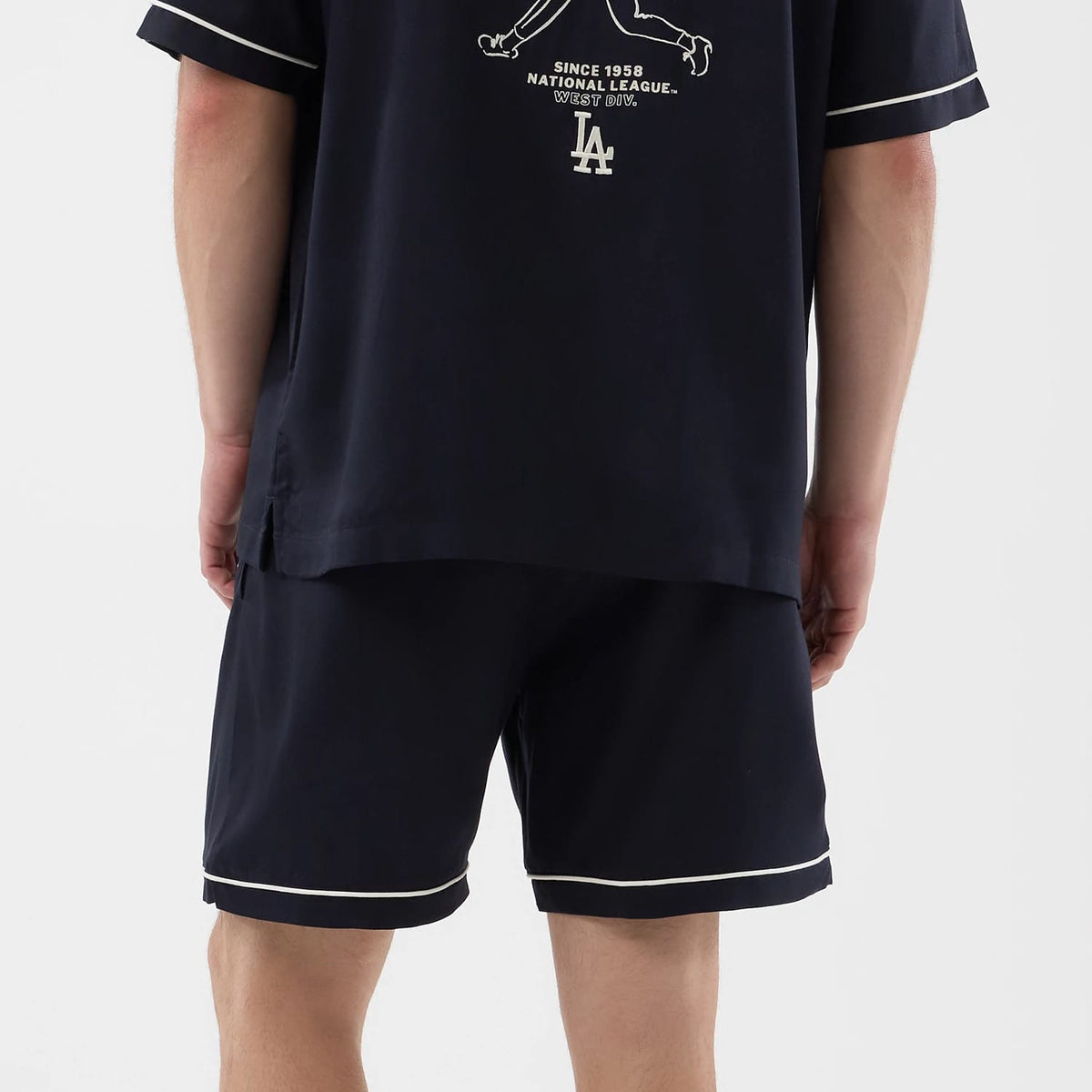 New Era LA Dodgers MLB Woven Navy Shorts, back view on a model paired with a matching top showing the shorts' dark navy colour, white piping along the hem, and a relaxed fit sitting above the knees.
