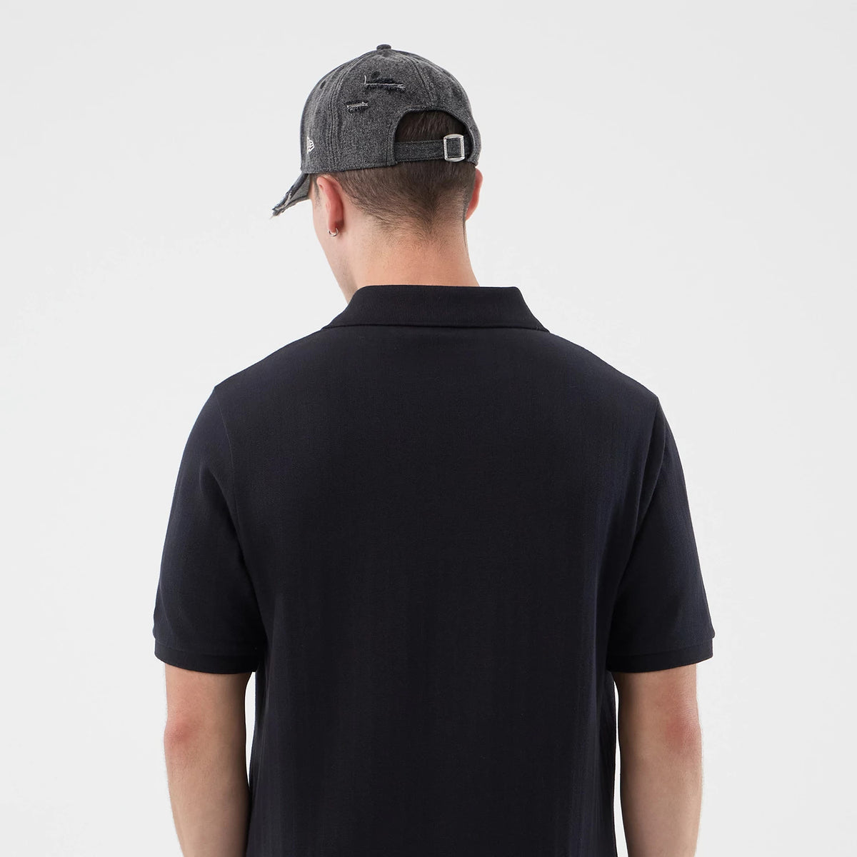 New Era New York Yankees MLB Rib Navy Polo T-Shirt, back view on a model with a grey cap, showcasing the plain navy canvas of the polo and a flat collar, with short sleeves and a straight hem.