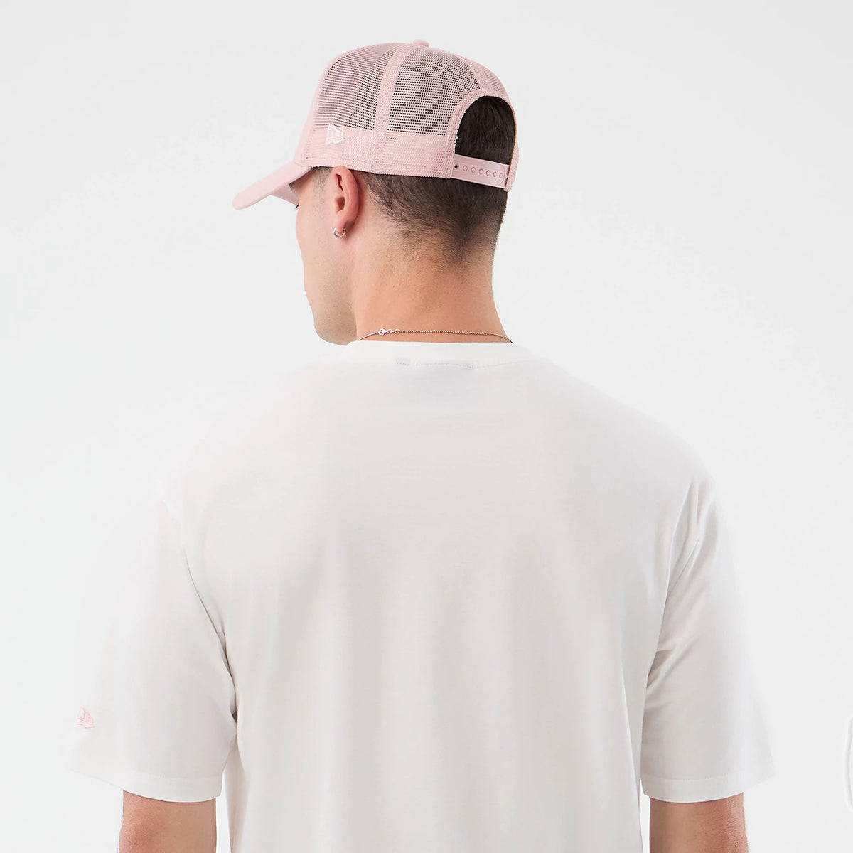 New Era New York Yankees MLB Midi League Essential White Oversized T-Shirt, back view on-model highlighting a plain white back with a small printed New Era logo on the sleeve, styled with a pale pink cap featuring an embroidered logo and eyelets.