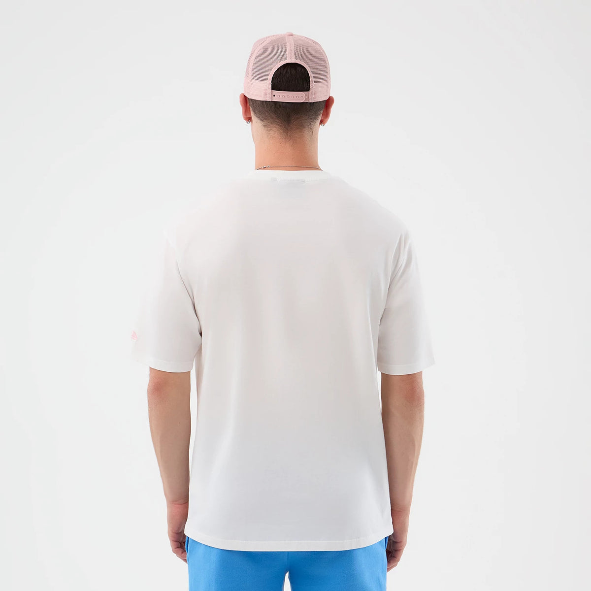 New Era New York Yankees MLB Midi League Essential White Oversized T-Shirt, back view on a model with a pink mesh cap, showing the plain white back of the T-shirt extending to the sleeves and the New Era embroidered logo on the left sleeve.