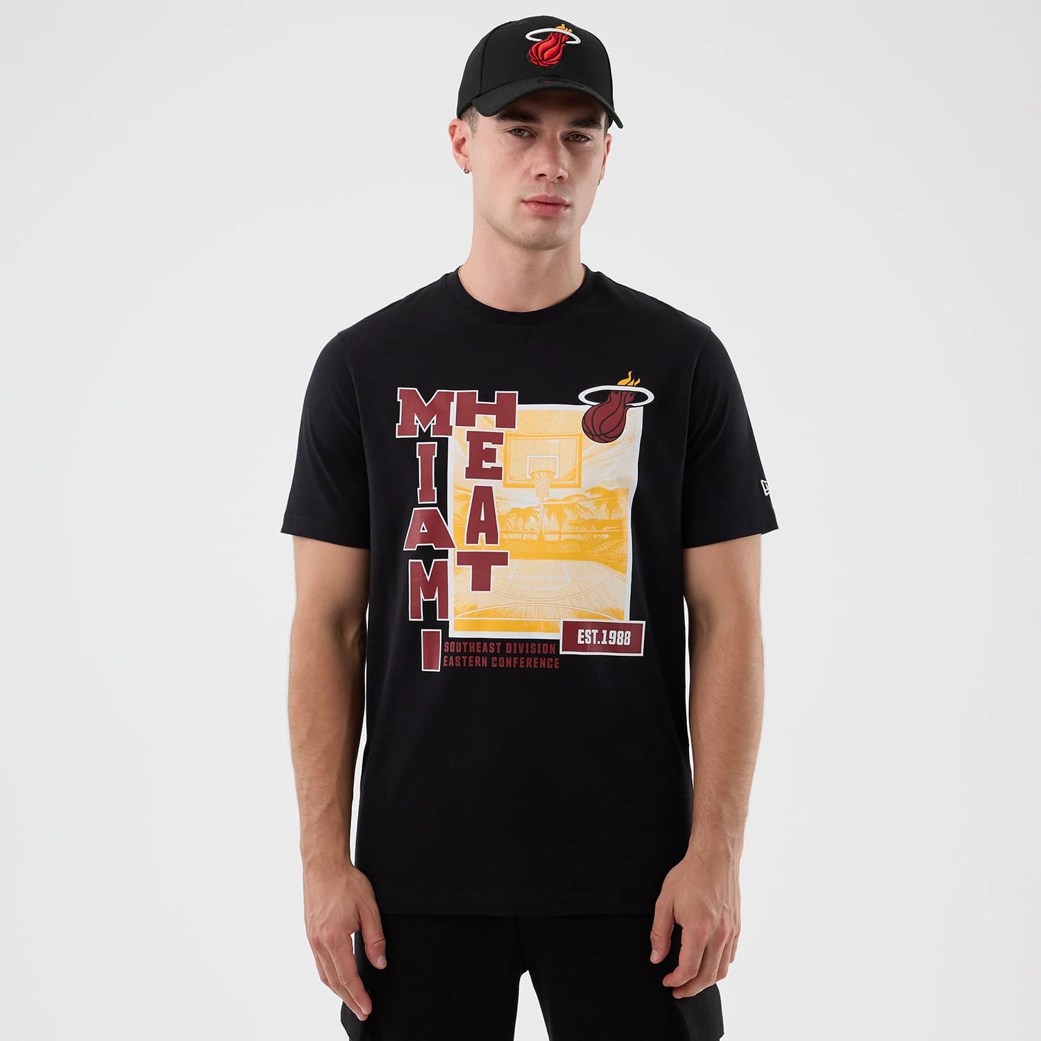 New Era Miami Heat NBA Graphic Black T-Shirt, front view on-model showcasing a graphic with Miami Heat lettering in red and yellow, a basketball court illustration, the Heat logo above, and a small New Era logo embroidered on the left sleeve.