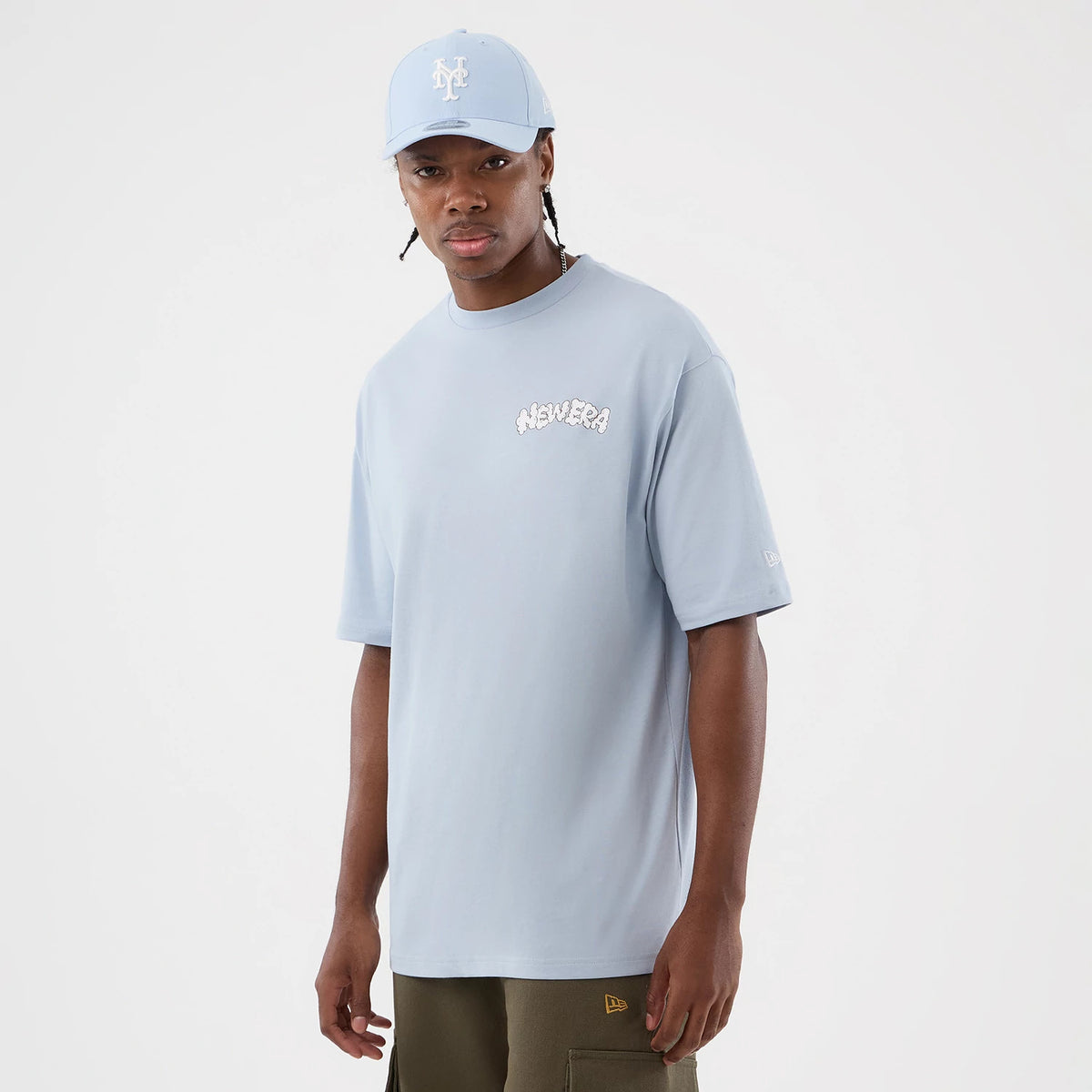 New Era Fun Block Party Graphic Pastel Blue Oversized T-Shirt, front view on a model wearing a matching pastel blue cap, showcasing a printed New Era logo on the chest, a embroidered logo on the sleeve, and relaxed short sleeves.