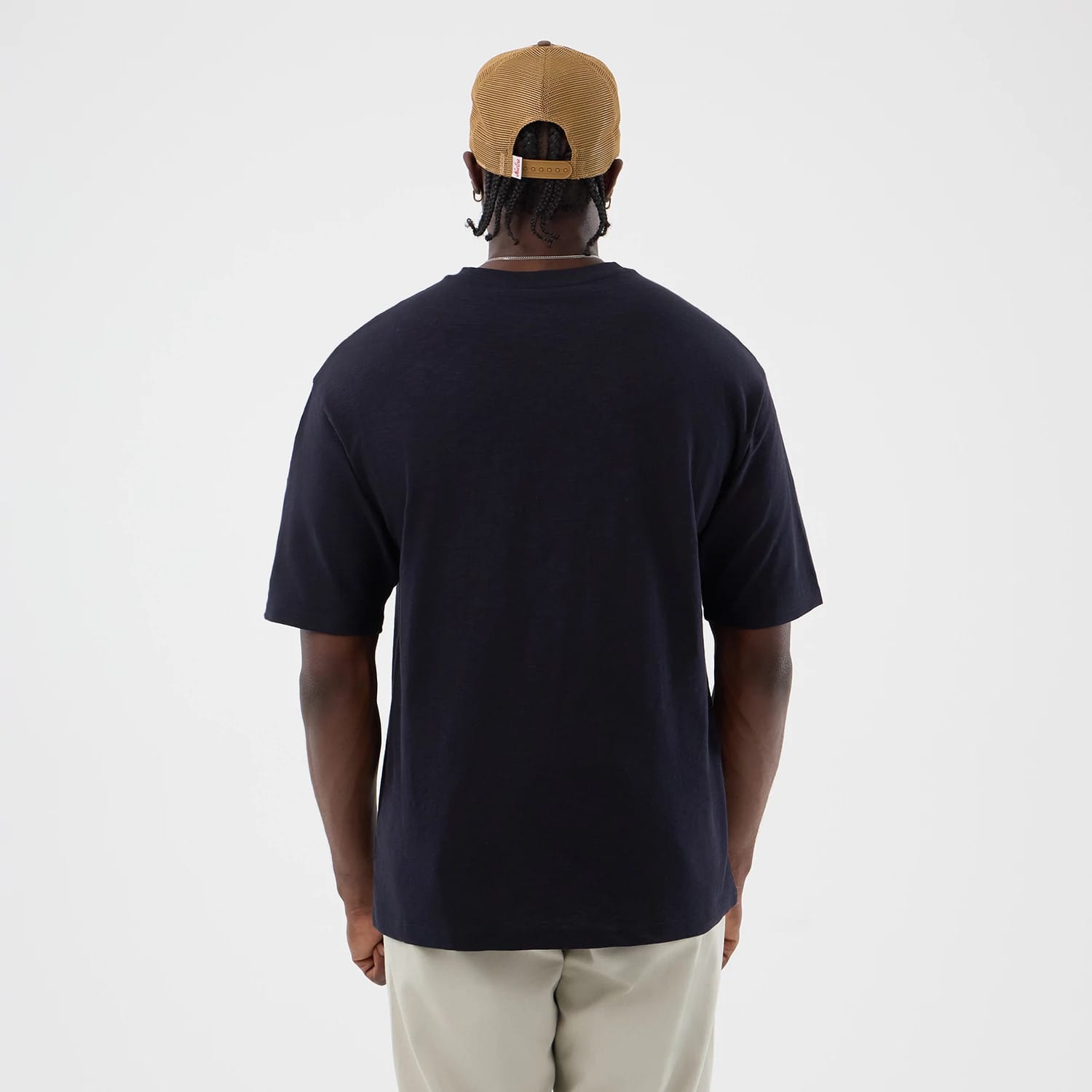 New Era Slub Navy Oversized T-Shirt, back view on a model wearing beige trousers and a tan cap, showing the plain navy back with short sleeves ending at the elbow, providing a clean and simple aesthetic.