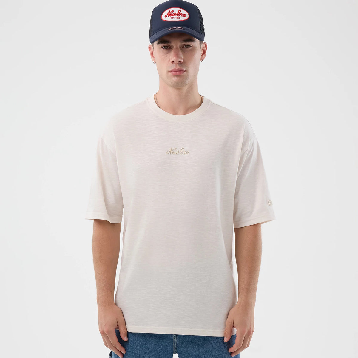 New Era Slub Open White Oversized T-Shirt, front view on-model displaying the soft white oversized silhouette with a embroidered New Era script logo on the chest and a small embroidered logo on the left sleeve, styled casually with jeans.
