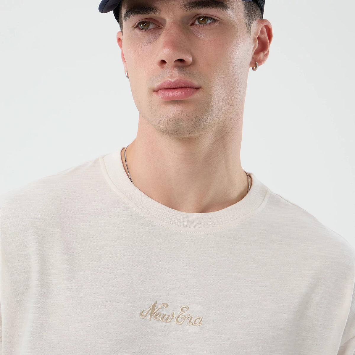 New Era Slub Open White Oversized T-Shirt, front view on a model, displaying the soft white fabric with a beige embroidered New Era logo centred on the chest, the slightly wider crew neckline and relaxed fit complementing a casual style.