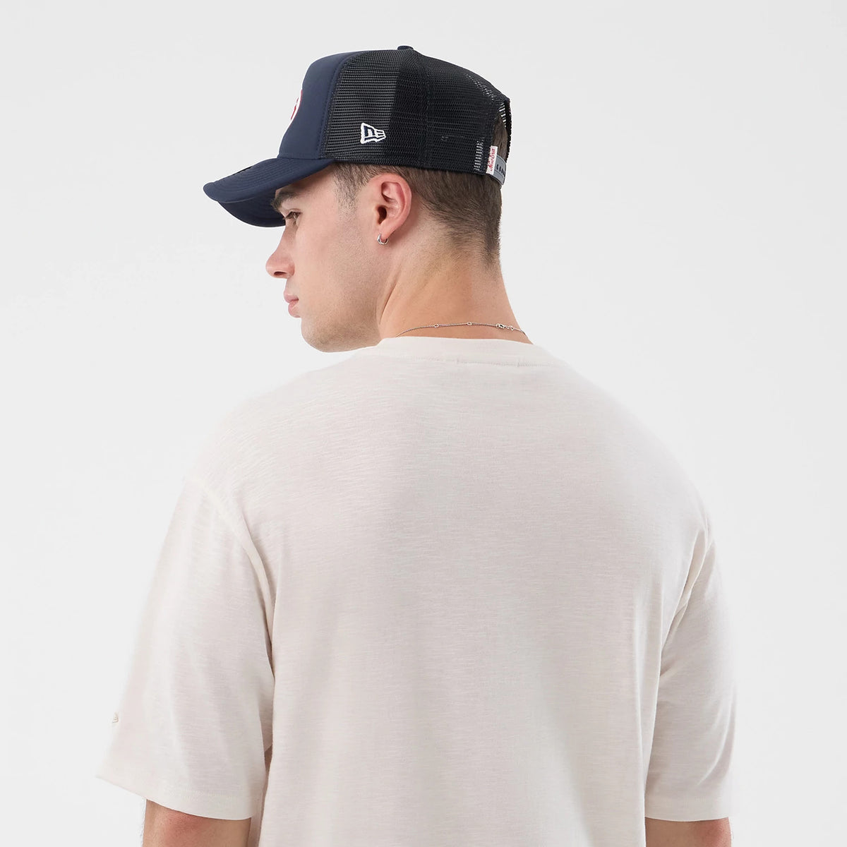 New Era Slub Open White Oversized T-Shirt, back view on a model with a black New Era cap, showing the plain white slub texture of the shirt, short sleeves, and wide collar, complemented by the cap’s embroidered New Era logo on the side.