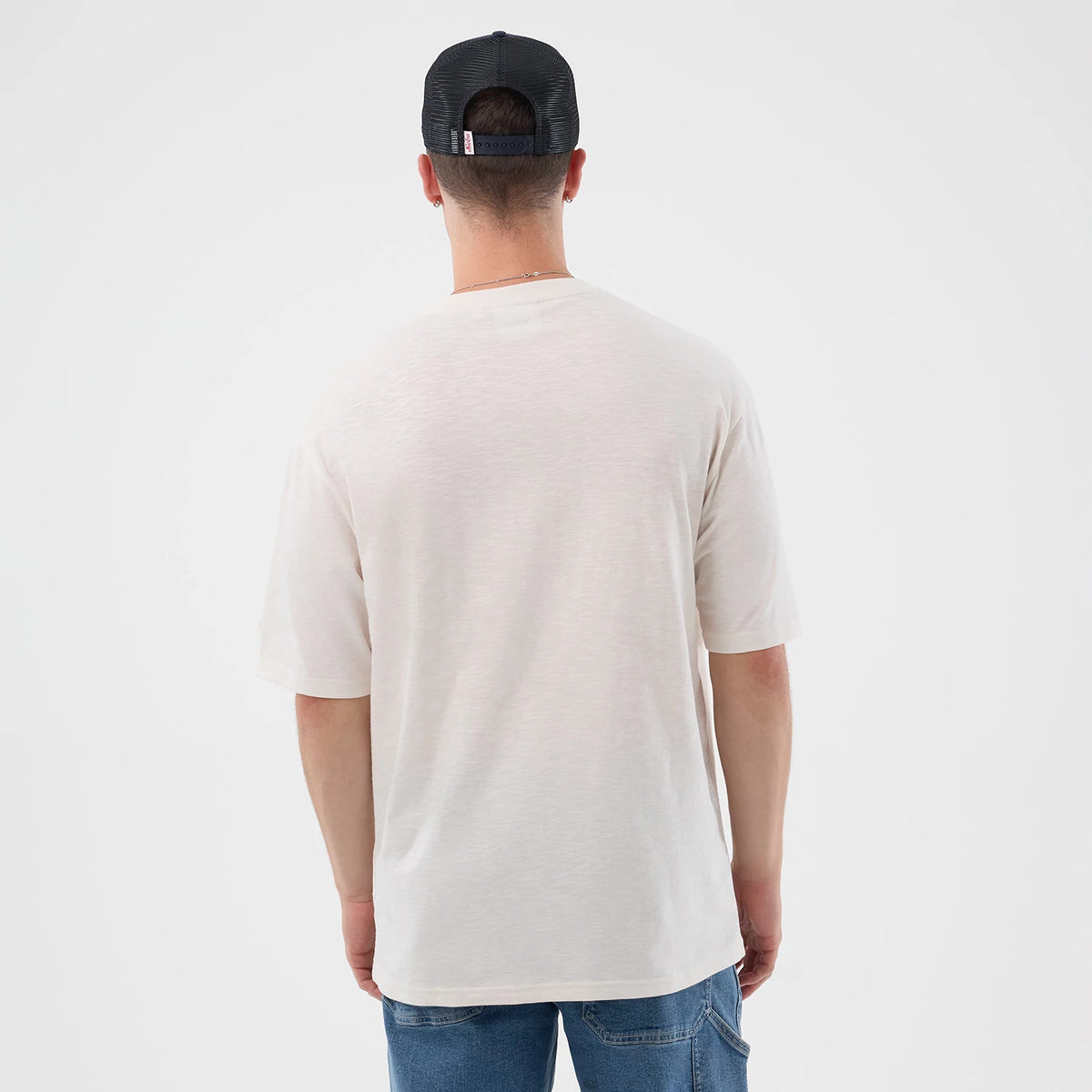 New Era Slub Open White Oversized T-Shirt, back view on a model showing the plain white slub texture with short sleeves, the loose fit draping over jeans, and a black cap worn, emphasising a casual and relaxed style.