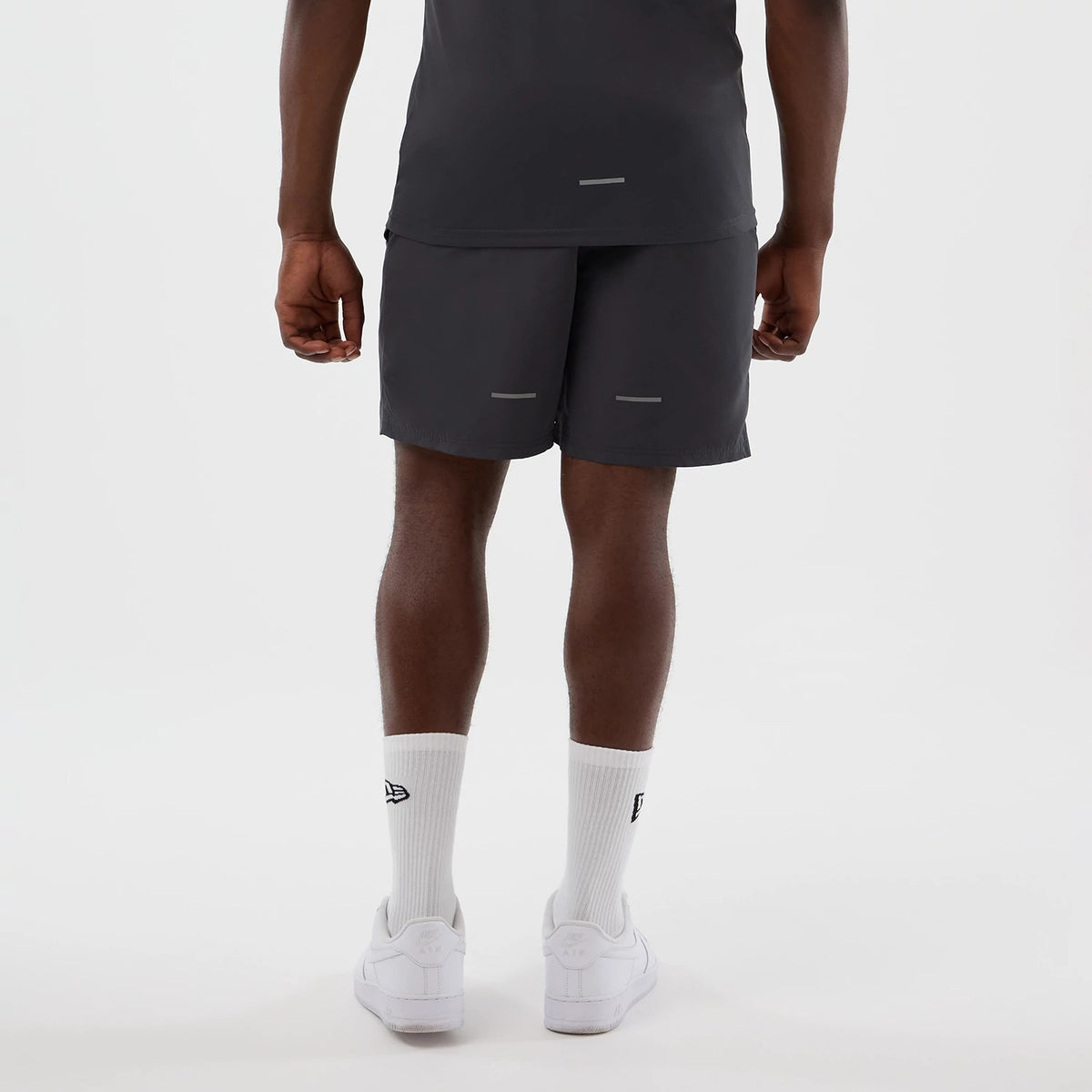 New Era New York Yankees MLB Core Plus Dark Grey Shorts, back view on a model showing the plain dark grey design with horizontal reflective strips on each leg, paired with white New Era branded socks and plain white trainers.