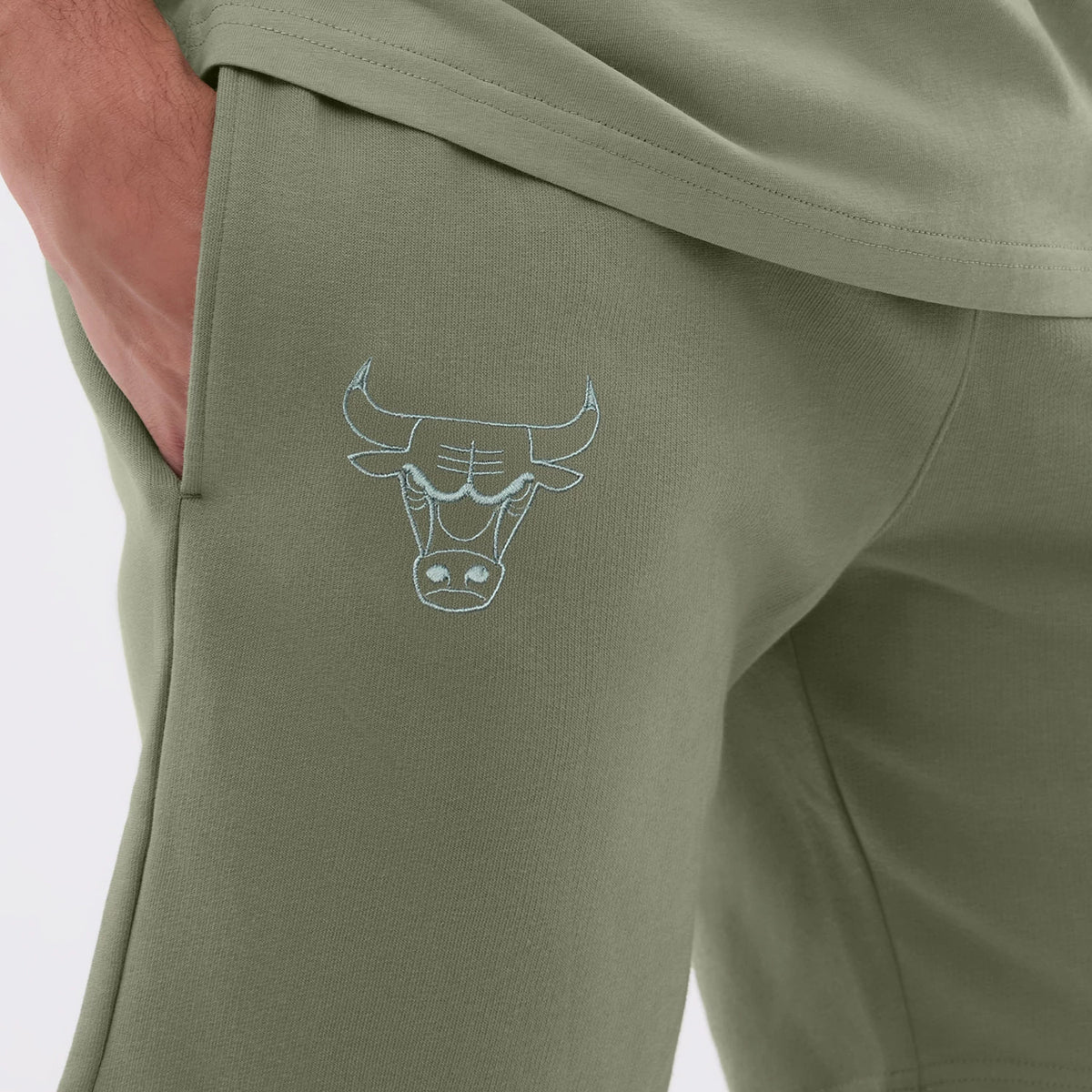 New Era Chicago Bulls NBA League Essential Pastel Green Shorts, side view showing a pale blue embroidered Chicago Bulls logo near the pocket, a relaxed fit with topstitching, styled casually with a matching pastel green top.