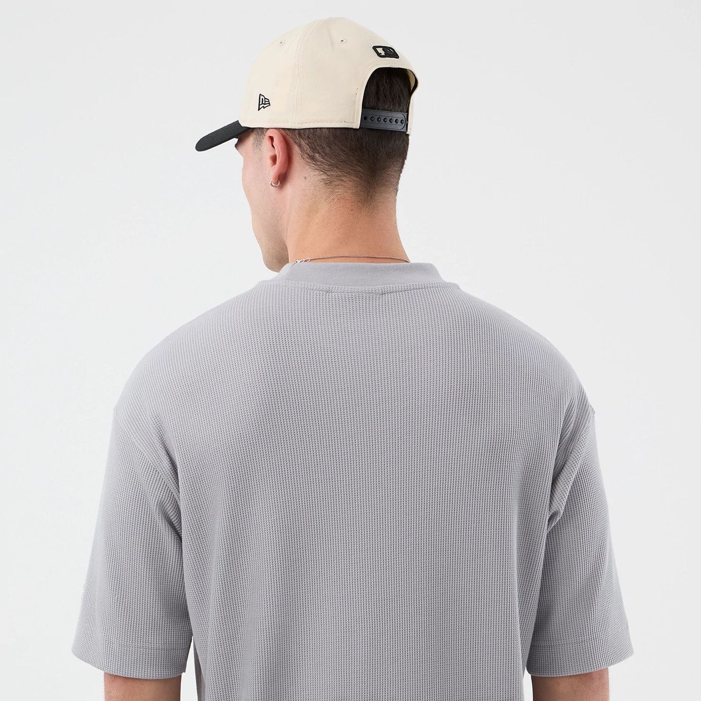 New Era New York Mets MLB Waffle Grey T-Shirt, back view on-model displaying the simple grey waffle texture and relaxed fit with short sleeves, paired with a beige cap featuring an embroidered New Era logo on the side and snapback closure.