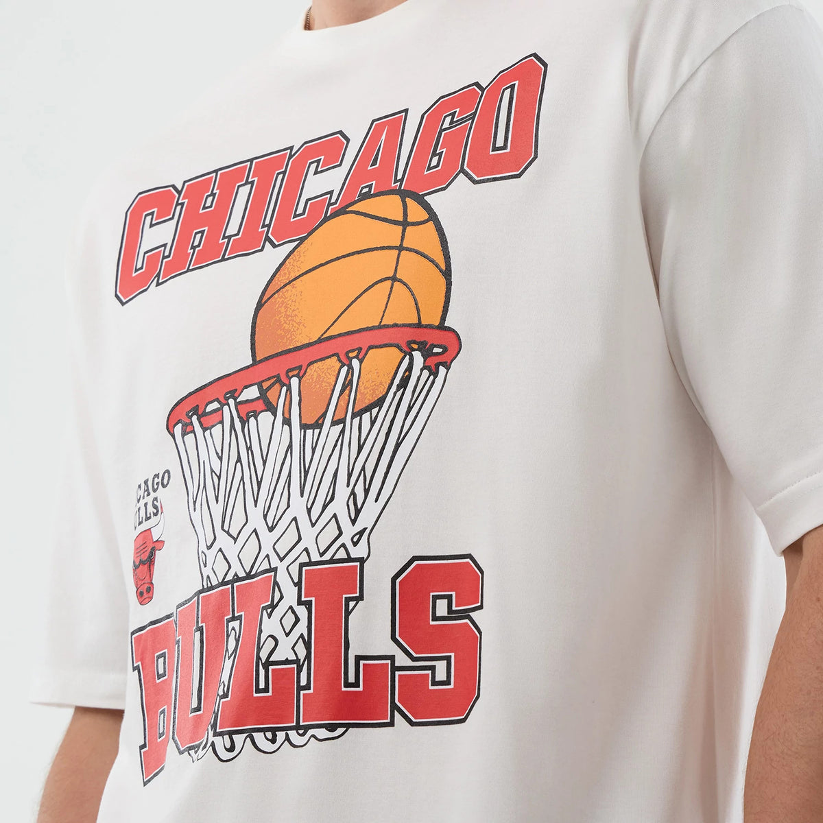 New Era Chicago Bulls NBA Basketball Graphic White Oversized T-Shirt, front view showing a red CHICAGO BULLS logo above and below an illustrated orange basketball going through a hoop, with a small Bulls logo printed on the left side.
