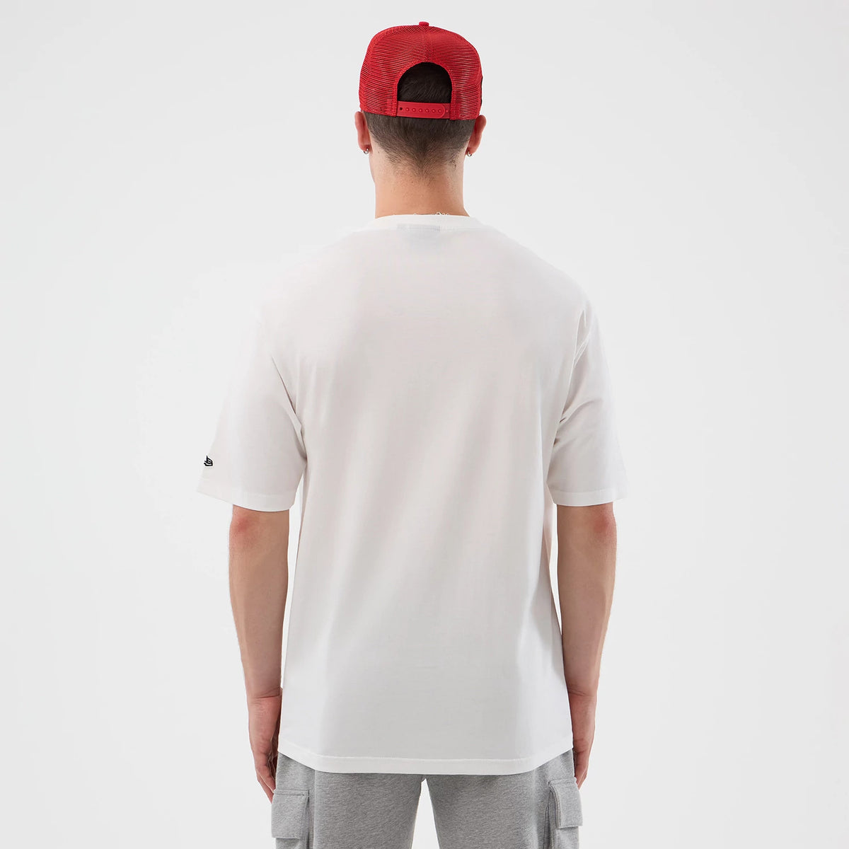 New Era Chicago Bulls NBA Basketball Graphic White Oversized T-Shirt, back view on a model showing the plain white back with no graphics, an embroidered New Era logo on the left sleeve, and loose fit styling over grey cargo shorts.
