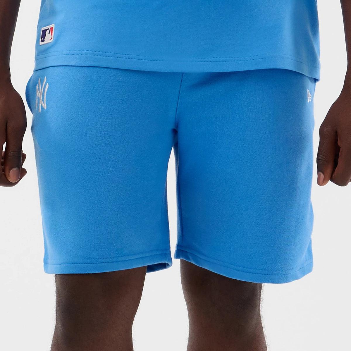 New Era New York Yankees MLB League Essential Pastel Blue Shorts, front view on model showing the soft blue fabric with an embroidered white Yankees logo on the left thigh, a small New Era logo on the right leg.