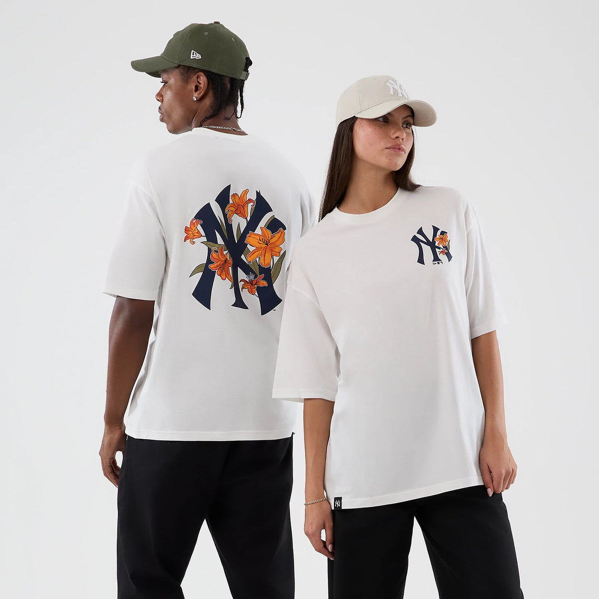 New Era New York Yankees MLB Floral White Oversized T-Shirt, on-model view featuring a navy Yankees logo adorned with orange floral motifs on the back, and a smaller matching logo on the front, styled with contrasting black trousers.
