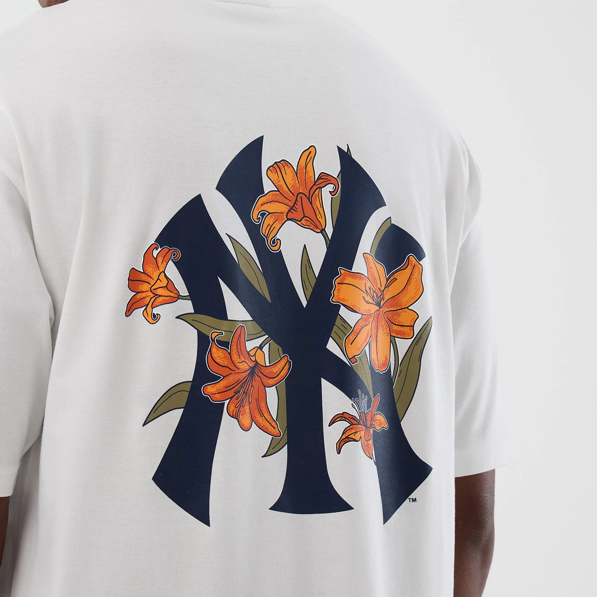 New Era New York Yankees MLB Floral White Oversized T-Shirt, back view showing a large navy blue Yankees logo adorned with orange lilies and green leaves, centrally positioned on the oversized white fabric of the shirt.