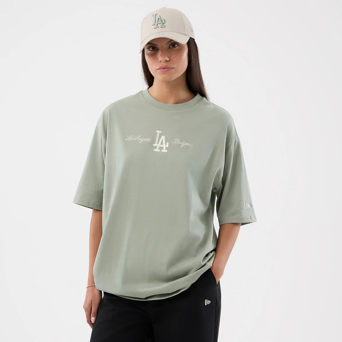 New Era LA Dodgers MLB Script Pastel Green Oversized T-Shirt, front view on a model, featuring a large printed LA logo in white across the chest, script text, and a small embroidered New Era logo on the left sleeve, paired with a light cap.