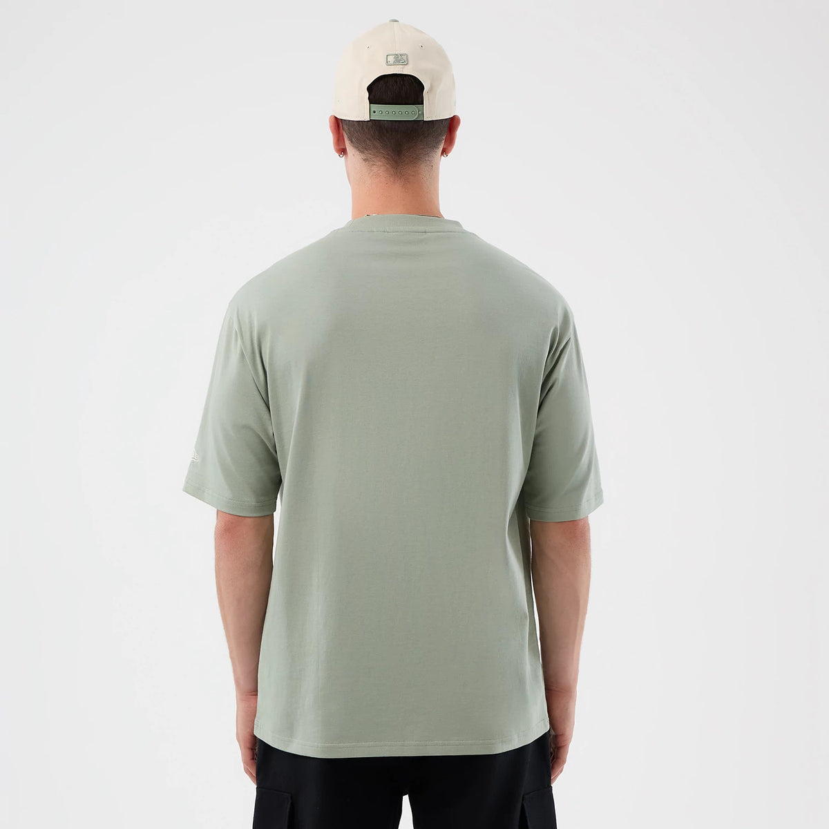 New Era LA Dodgers MLB Script Pastel Green Oversized T-Shirt, back view on model paired with a light cap, showing the plain pastel green back panel, relaxed fit sleeves draping just above the elbows, and a side logo near the left sleeve.