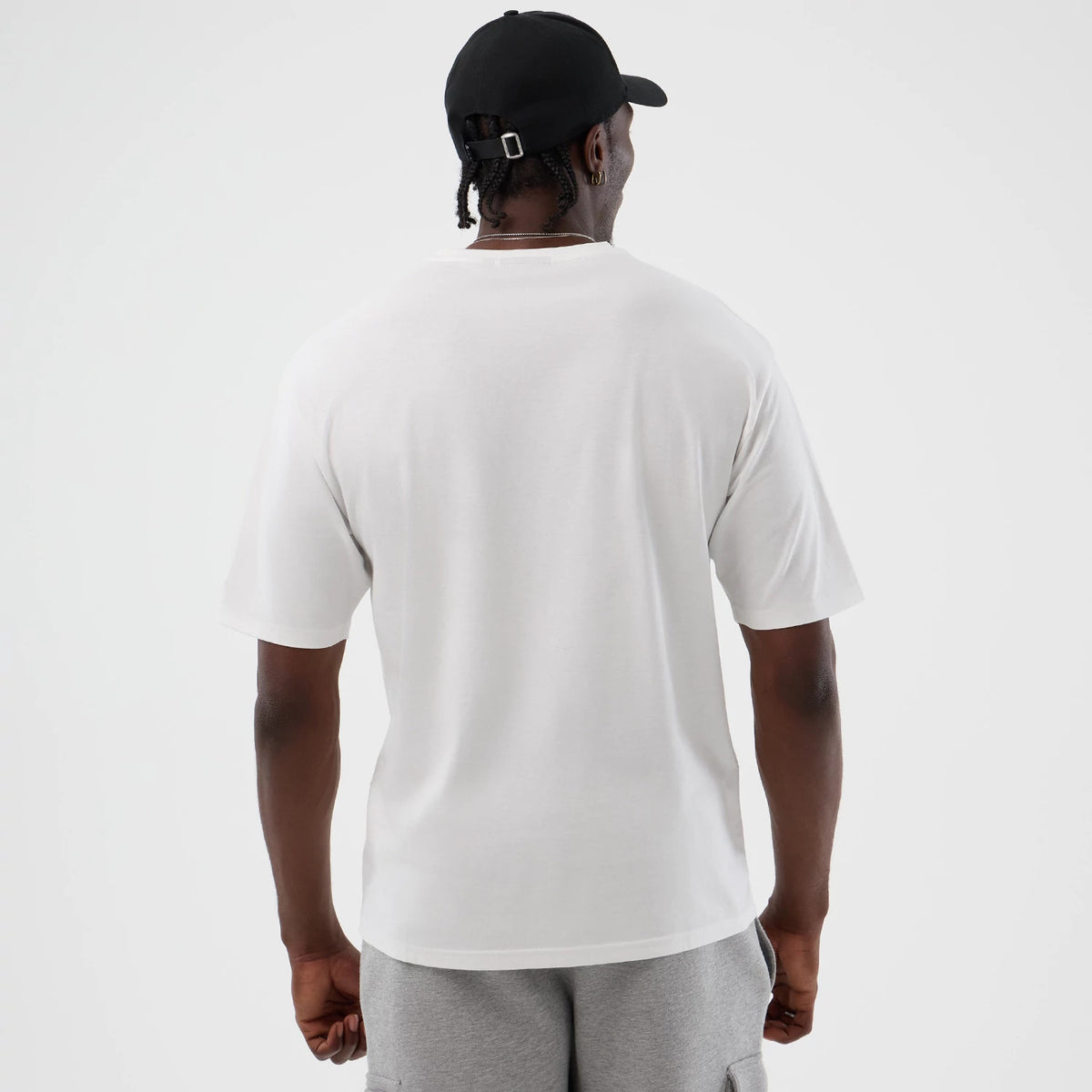 New Era New York Yankees MLB Icon Graphic White T-Shirt, back view on a model showing the plain white back with short sleeves, styled with a black cap and grey shorts, highlighting the simplicity and classic design of the t-shirt.
